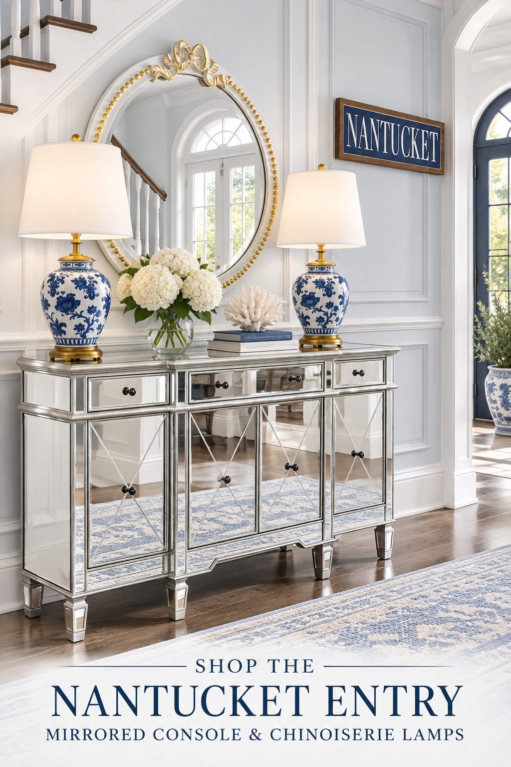 Elegant Nantucket entry with silver mirrored console, ivory and gold bow mirror, pair of blue and white chinoiserie lamps, white hydrangeas, coral, blue books, navy Nantucket sign and faded blue rug.