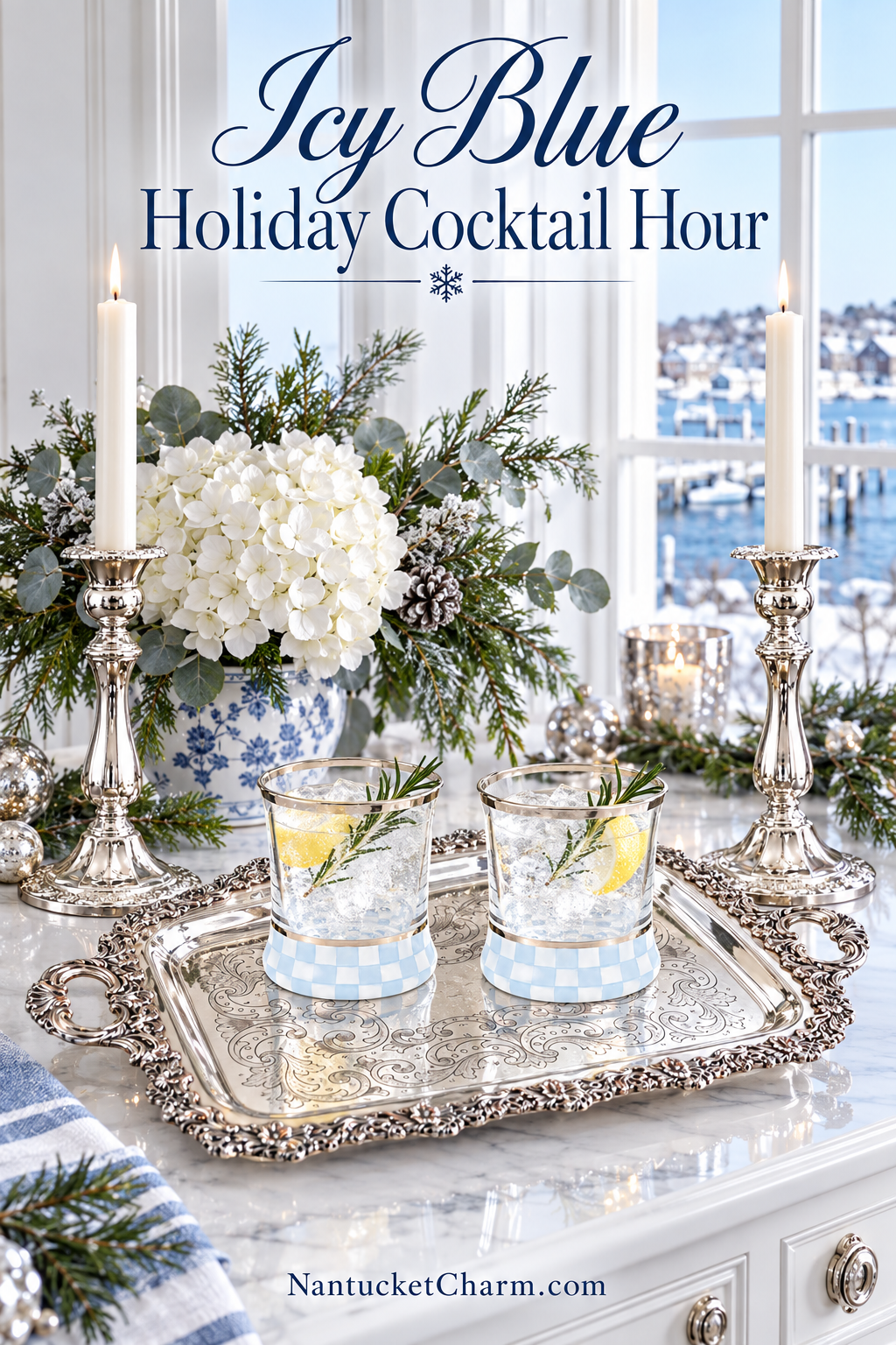 Two MacKenzie-Childs Sterling Check cocktail glasses with lemon and rosemary on an ornate silver tray, flanked by silver candlesticks, white hydrangeas in a blue-and-white chinoiserie planter and a snowy Nantucket harbor through the window.